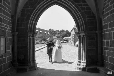 Photo de mariage : la mariée arrive à l'église au bras de son père - Photographe Nathalie Courau-Roudier