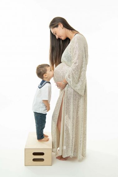 Photo studio de grossesse, le grand frère fait un bisou au ventre de la Maman