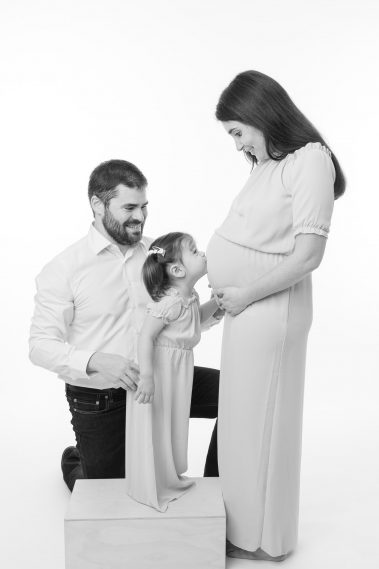 Photo studio de grossesse, la grande soeur fait un bisou au ventre de maman