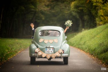 journée de mariage : les mariés saluent dans leur voiture - Photographe Nathalie Courau-Roudier