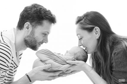 Photo studio Naissance, papa et maman portent leur bébé en contre-jour