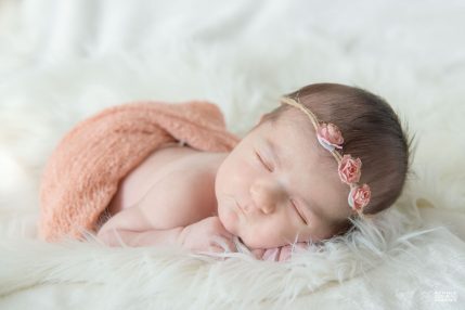 Photo studio Naissance, nouveau-né sur une couverture blanche avec des roses dans les cheveux