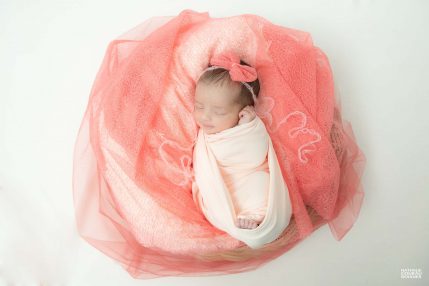 Photo studio Naissance, bébé emmailloté dans une corbeille habillée de tulle corail